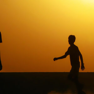 Silhouette of boys playing football against a warm sunrise sky.