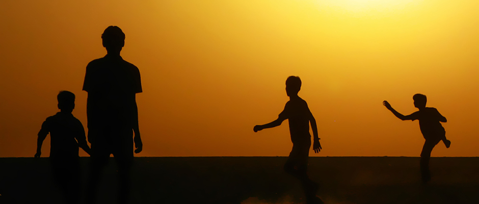 Silhouette of boys playing football against a warm sunrise sky.